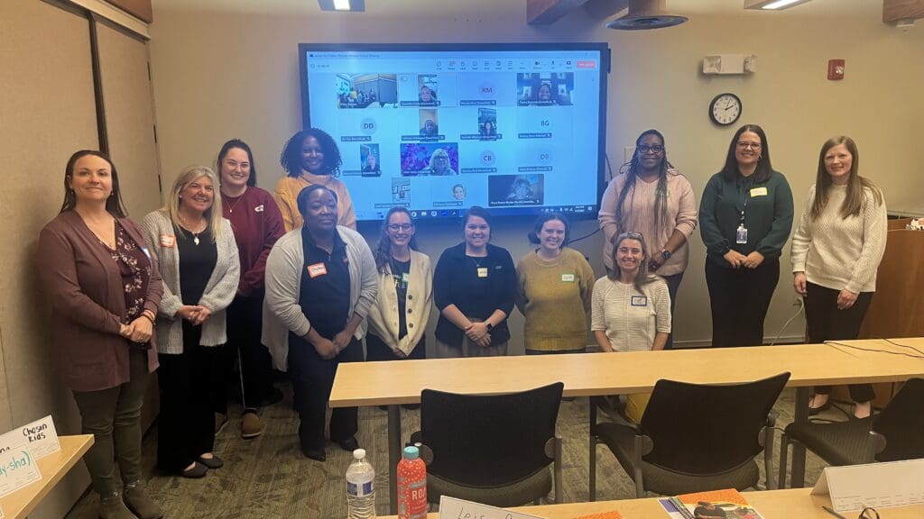 A group of Action for Children staff and Provider Advisory Council members standing together during a hybrid meeting.