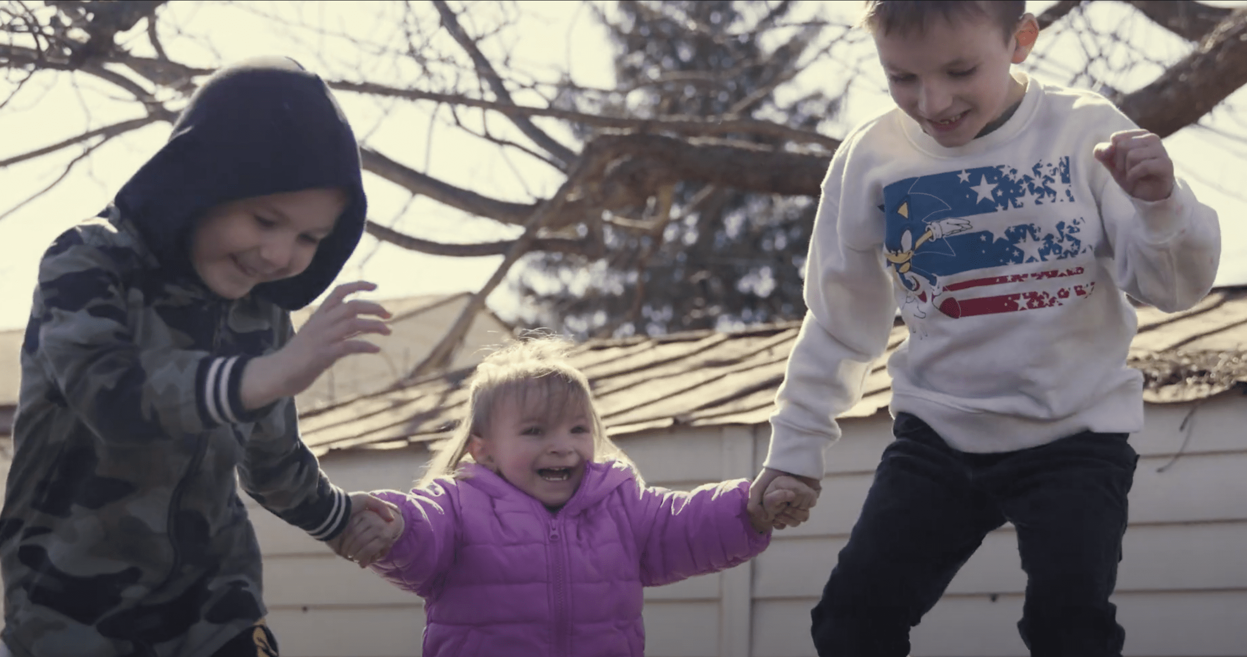 Tia’s three children smiling and playing on a trampoline after a Help Me Grow home visit